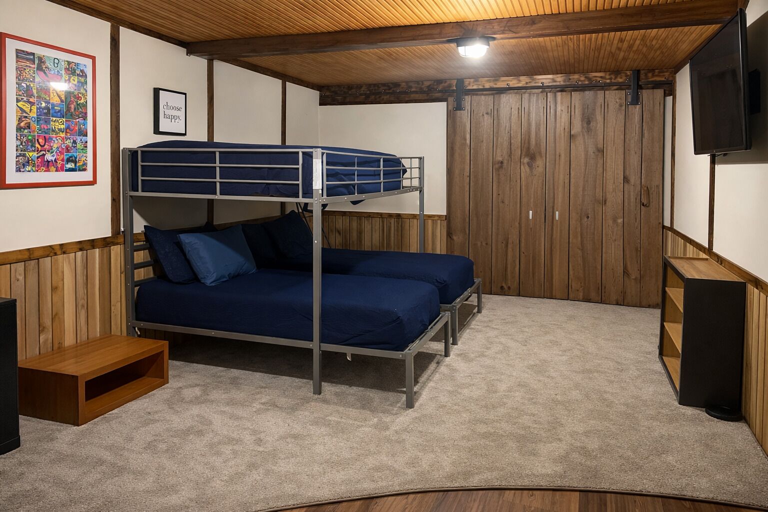 A bunk bed room with a wooden ceiling, a framed picture on the wall, and a television mounted on the wall.