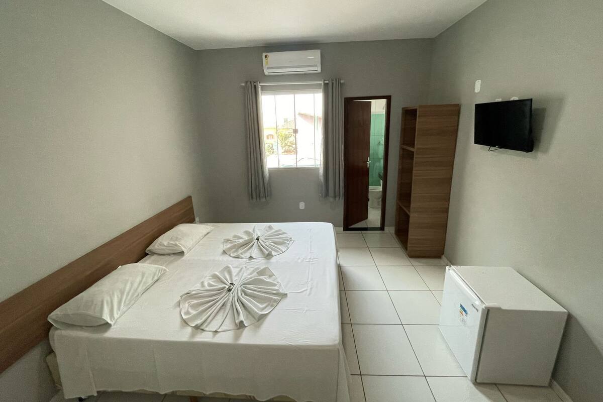 Una habitación de hotel con una cama, televisor, armario y aire acondicionado.