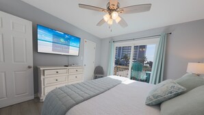A bedroom with a bed, a ceiling fan, a TV on the wall, and a view of the outdoors. - Sand Dollar 5 – Your Bright & Breezy East Beach Getaway!  Free Daily Activities! (Gulf Shores)