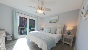 A bedroom with a bed, a nightstand, a ceiling fan, a window with curtains, and a balcony. - Sand Dollar 5 – Your Bright & Breezy East Beach Getaway!  Free Daily Activities! (Gulf Shores)