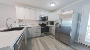 A modern kitchen with white cabinets, stainless steel appliances, and a wooden floor. - Sand Dollar 5 – Your Bright & Breezy East Beach Getaway!  Free Daily Activities! (Gulf Shores)