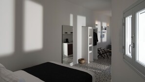 A bedroom with a bed, a small desk, a chair, and a kitchenette in the background. - ORANA Residence Santorini (Thira - Santorini)