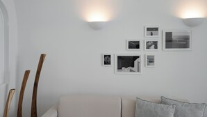 A modern living room with a sofa, decorative wooden sticks, and wall-mounted picture frames. - ORANA Residence Santorini (Thira - Santorini)
