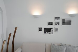 A modern living room with a sofa, decorative wooden sticks, and wall-mounted picture frames. - ORANA Residence Santorini (Thira - Santorini)