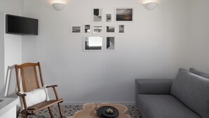 Un salon moderne avec un canapé gris, une chaise en bois, un téléviseur à écran plat et des cadres photos accrochés au mur.