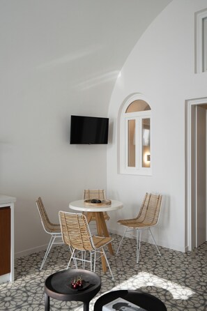 A dining area with a round table, four wicker chairs, a flat-screen TV mounted on the wall, and a patterned floor.