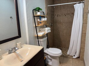 Une salle de bain équipée d’un lavabo, de toilettes et d’une douche. On y trouve des étagères avec des serviettes et des articles de toilette.