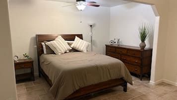 A bedroom with a bed, wooden headboard, bedside tables, a dresser, a ceiling fan, and a potted plant.