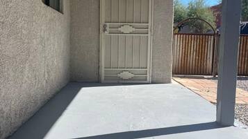 A covered patio area with a concrete floor and a white door with a decorative design.