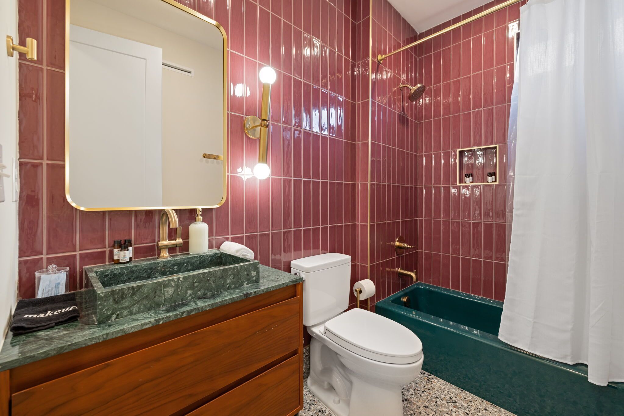 A bathroom with a marble vanity, a white toilet, a green bathtub, and a large mirror with lights.