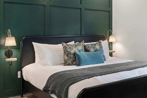 Un letto con una testiera scura, biancheria da letto bianca e cuscini decorativi. Due lampade a parete da ciascun lato del letto.