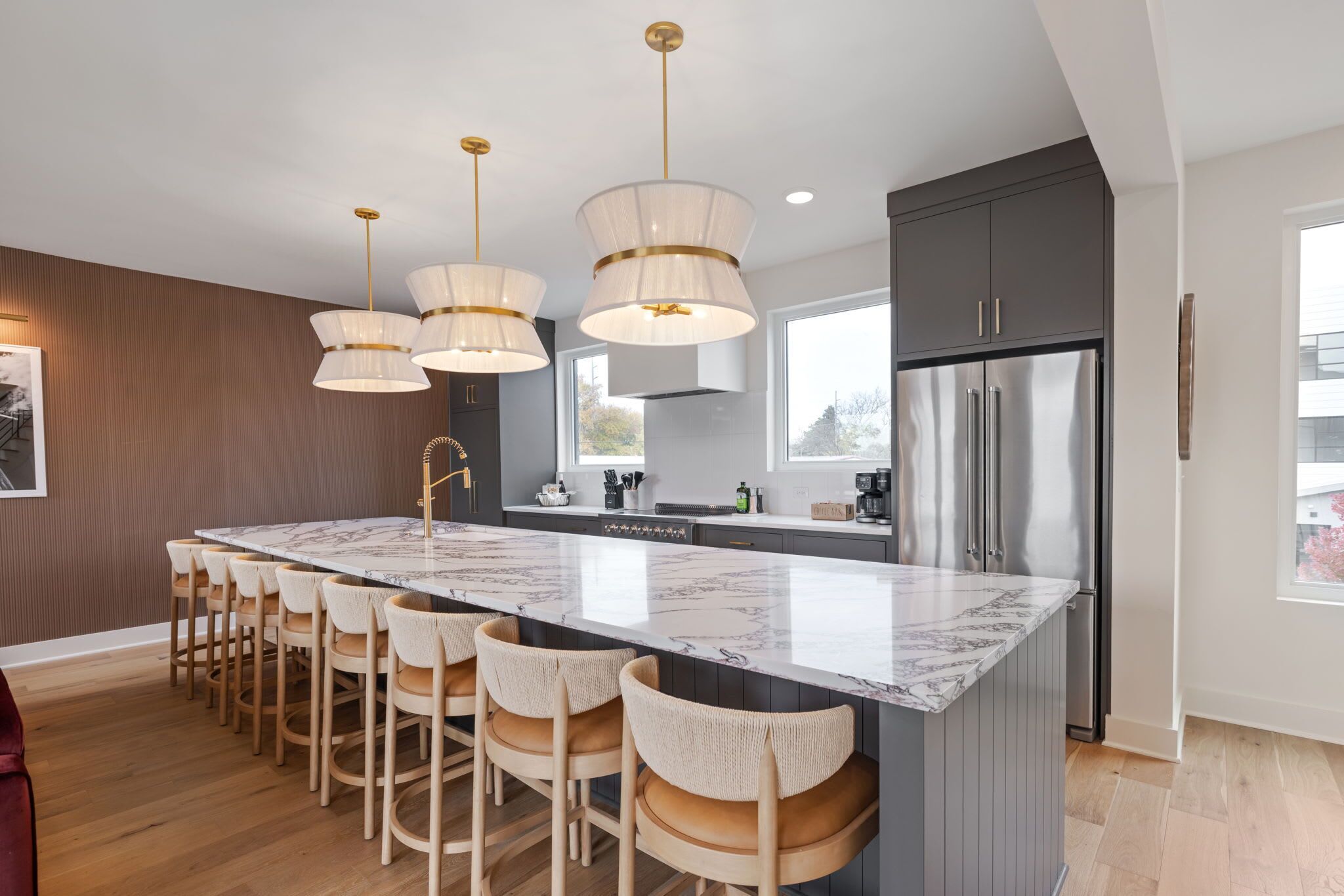 A modern kitchen with a large island, bar stools, stainless steel appliances, and pendant lighting.