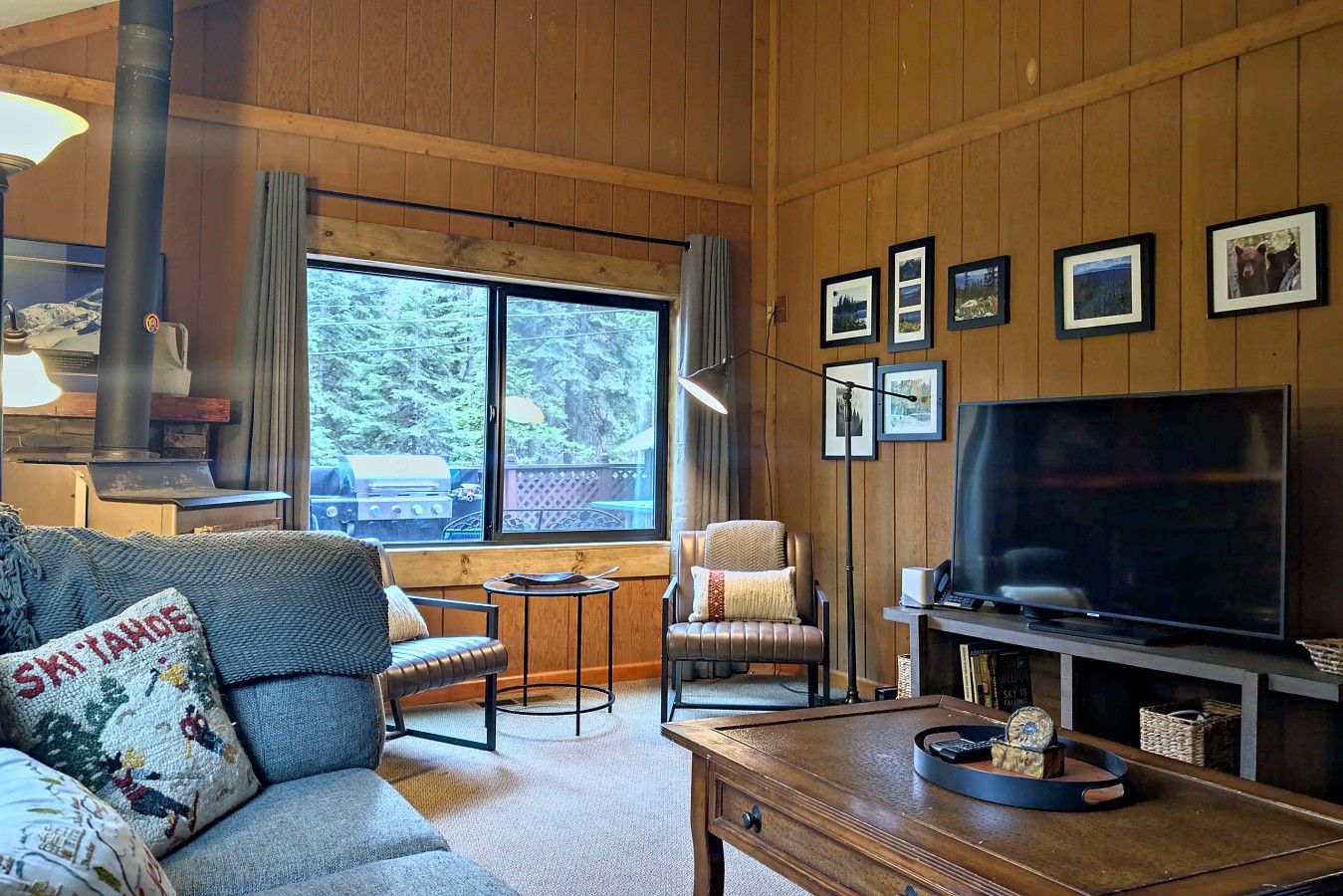 A cozy living room with a fireplace, a television, and a large window offering a view of the outdoors.