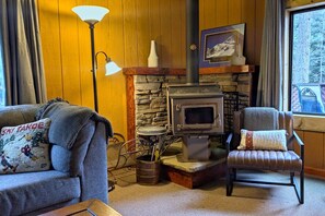 Een gezellige woonkamer met een stenen open haard, een bank, een fauteuil en een lamp.
