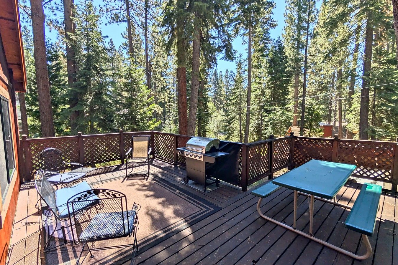 A deck with a grill, seating, and a view of a forest.