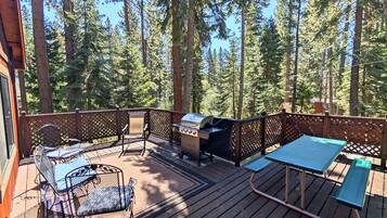 A deck with a grill, seating, and a view of a forest.