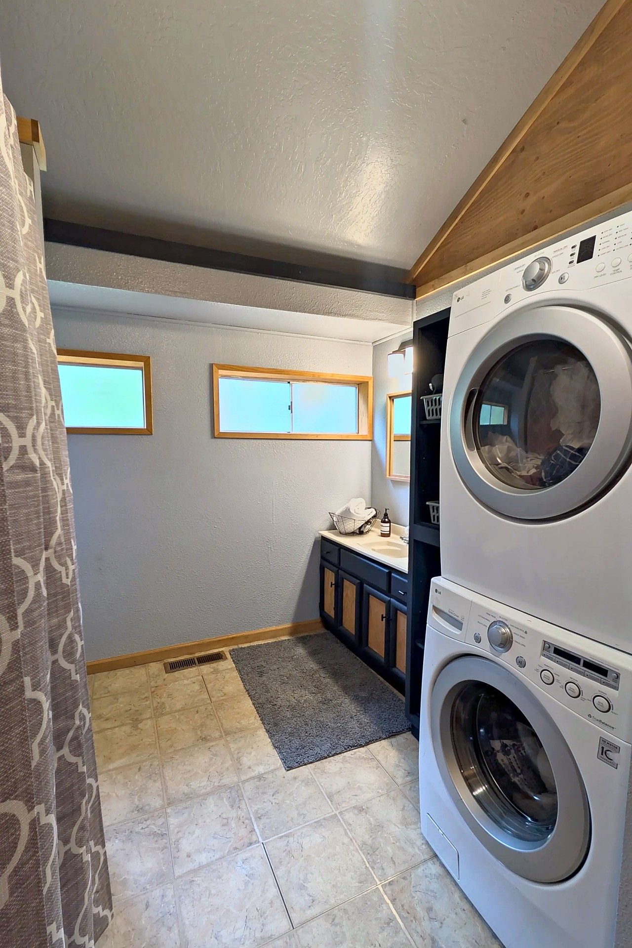 A laundry room with two stacked front-loading washing machines, a small sink, and a window.