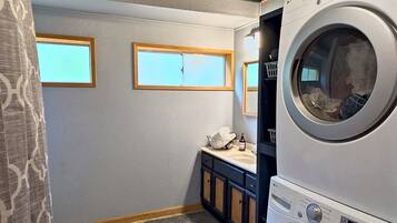 A laundry room with two stacked front-loading washing machines, a small sink, and a window.