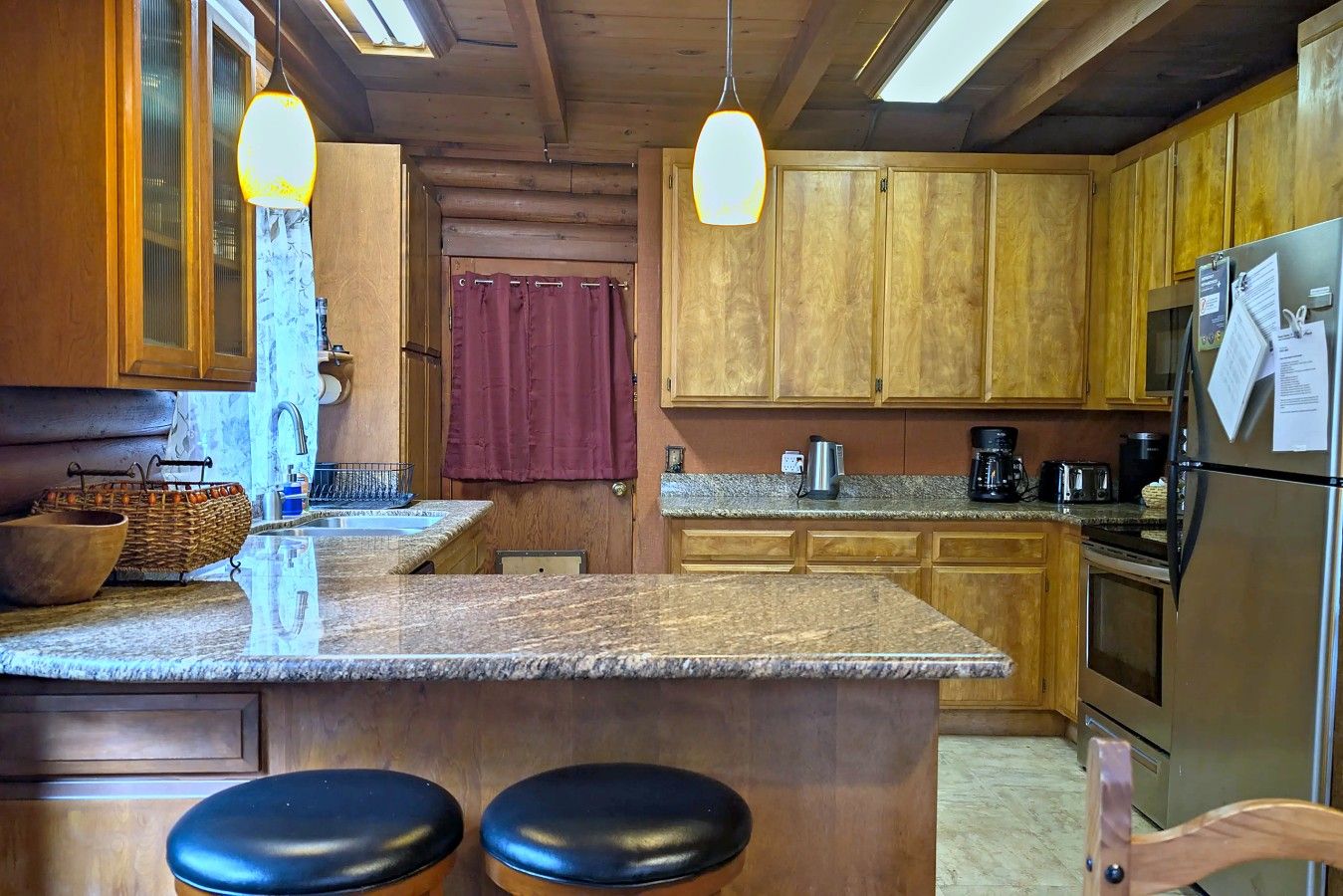 Una cocina con armarios de madera, encimera de granito, refrigerador de acero inoxidable y cafetera.