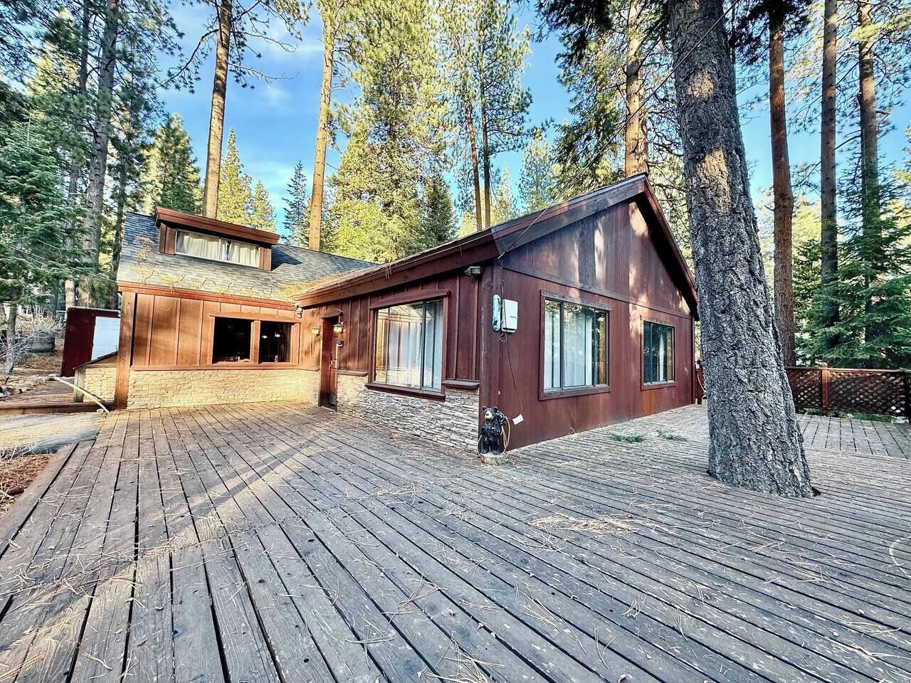 Une cabane dotée d’une terrasse en bois, entourée de grands arbres.