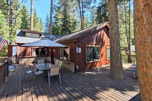 Une terrasse en bois avec des meubles d’extérieur, un patio couvert et une vue sur une zone boisée.