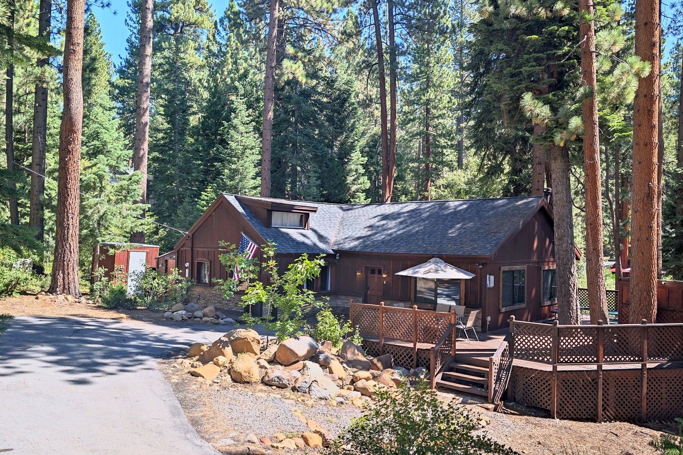 A lodge with a wooden exterior, a covered patio, and a view of tall pine trees.