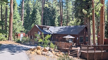 A lodge with a wooden exterior, a covered patio, and a view of tall pine trees.