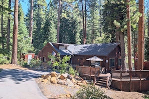 Un chalet avec une façade en bois, un patio couvert et une vue sur de grands pins.