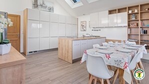 A modern kitchen with white cabinetry, a wooden island, and a dining area set for six. - Gîtes de France® Le cottage du parc (ROCQUEFORT)