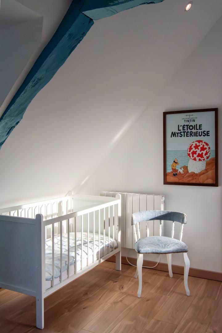 Et værelse med en hvid tremmeseng, en vintage stol og et billede på væggen.