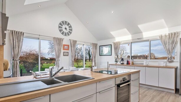 A modern kitchen with a large island, built-in appliances, and large windows offering a view of the outdoors. - Gîtes de France® Le cottage du parc (ROCQUEFORT)