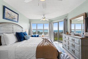 A bedroom with a bed, a dresser, a ceiling fan, a large window with a view, and a painting on the wall. - Emerald Towers West 1006 - Breezy Beachcomber (Fort Walton Beach)