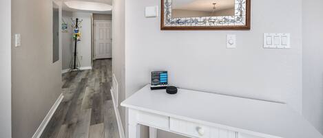 A hallway with a white desk, a mirror with a floral frame, and a door at the end.