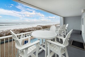 A balcony with a white table and chairs, overlooking a beach with a wooden boardwalk and a view of the ocean. - Islander 3005 - Gulf Secret (Fort Walton Beach)