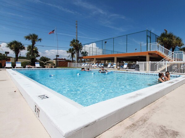 A swimming pool with lounge chairs and a flagpole with an American flag. - Surf Dweller 712 - Wave Whisperer (Fort Walton Beach)