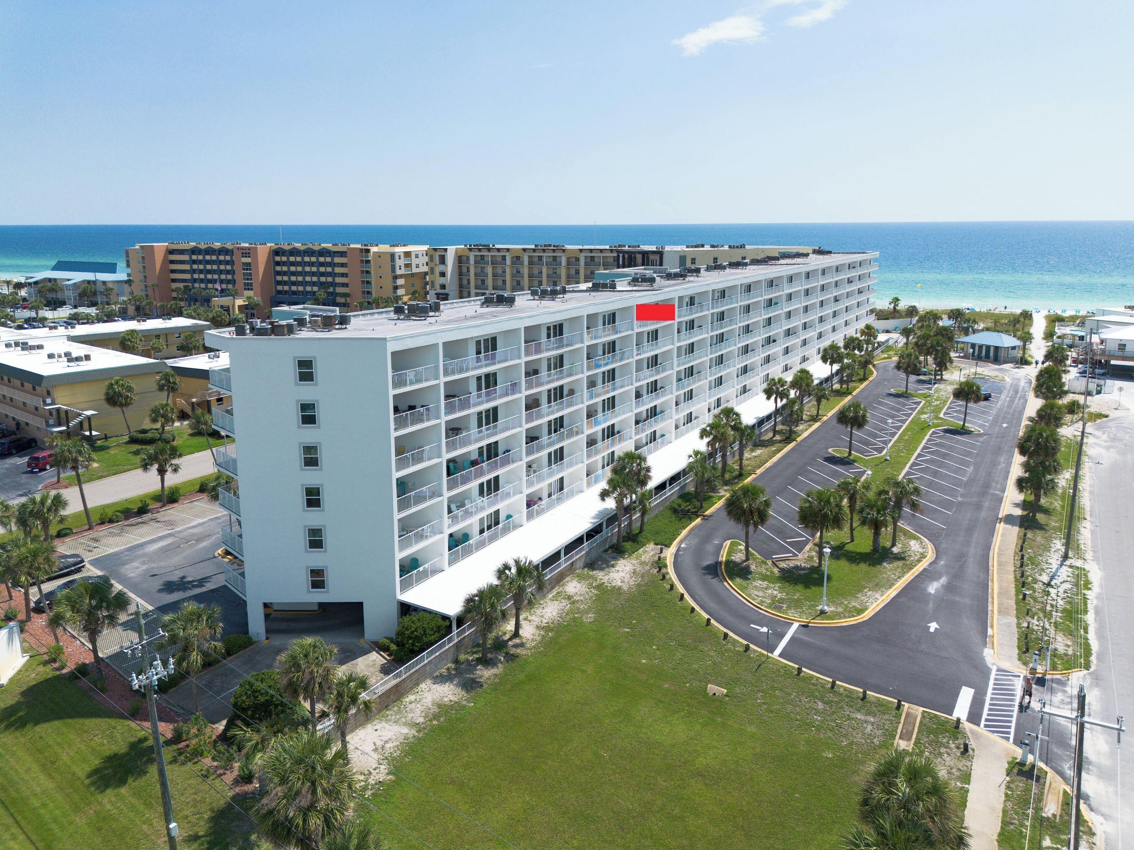 A multi-story hotel with a central courtyard, parking, and a view of the ocean.