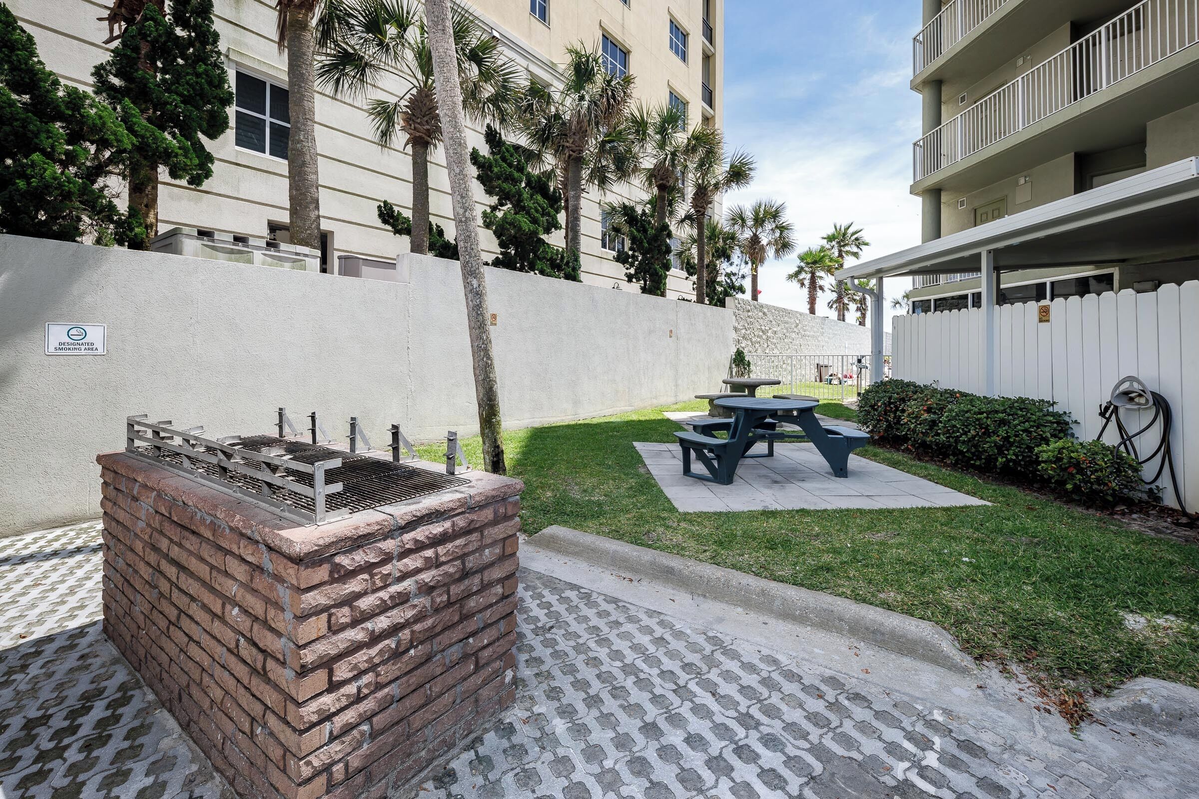 Un patio con una parrilla, una mesa de picnic y una valla blanca.