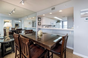 A dining area with a glass-top table, wooden chairs, and a lamp. - Seacrest 712 - Tidal Breeze (Fort Walton Beach)
