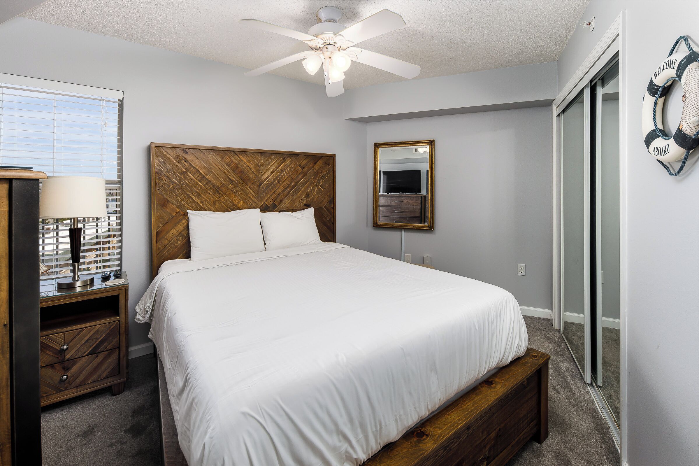 A bedroom with a bed, wooden headboard, a nightstand with a lamp, a mirror, and a sliding door.