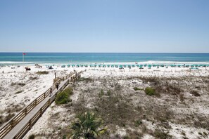 Une plage avec une promenade en bois menant au rivage, du sable blanc et une eau turquoise.