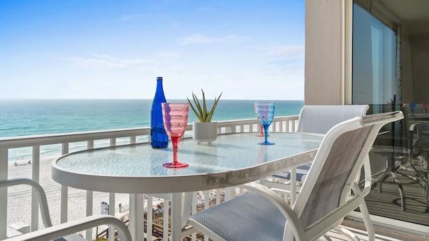 Un balcon avec une table en verre, deux chaises et une plante en pot.