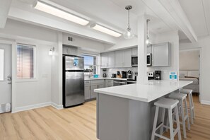 A modern kitchen with a central island, stainless steel appliances, and bar stools. - Coconut Beach House B (Fort Walton Beach)
