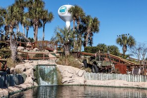 A water feature with a waterfall, palm trees, and a large water tower. - Coconut Beach House B (Fort Walton Beach)