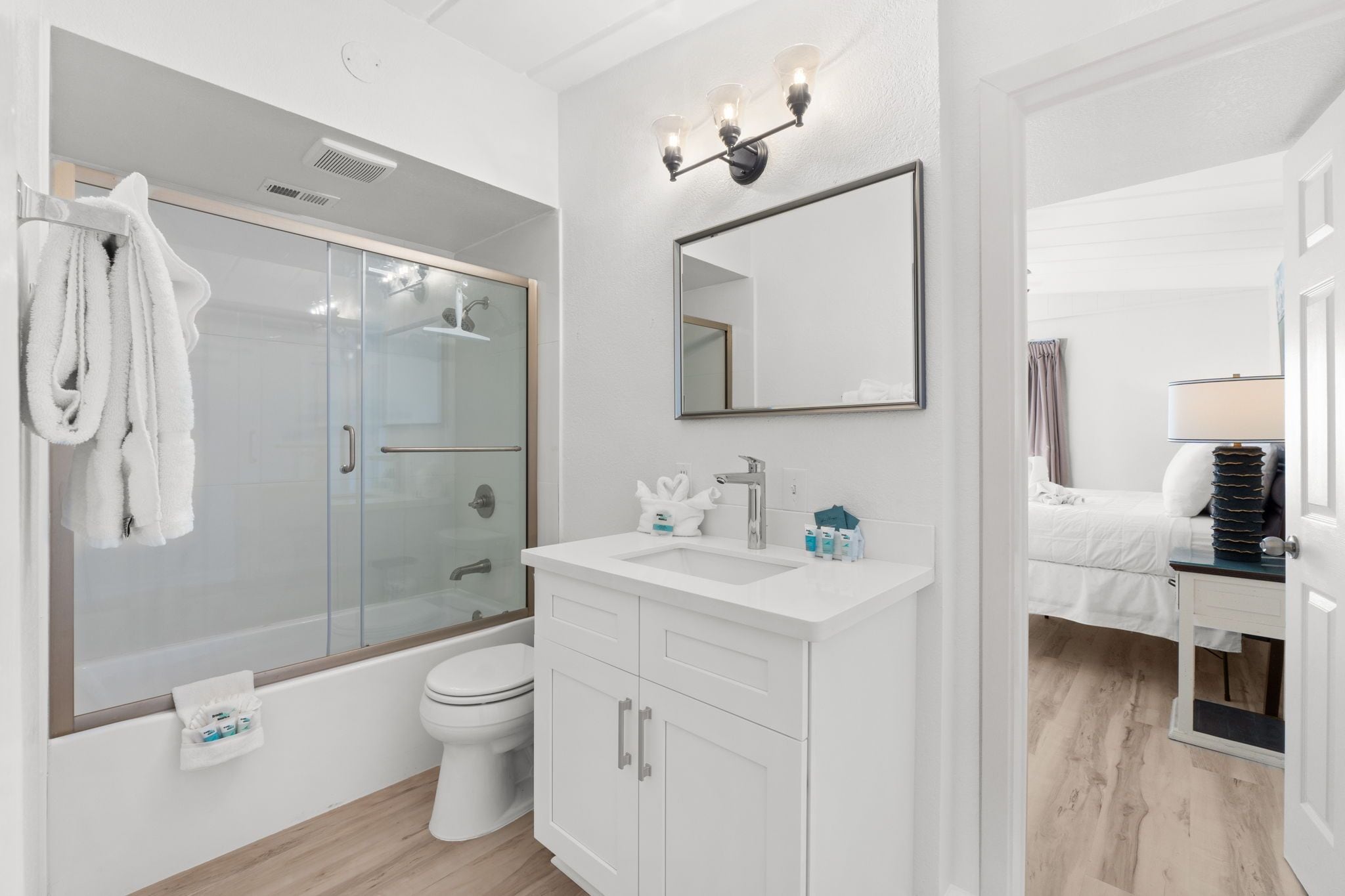Un baño moderno con ducha envuelta en cristal, un lavabo blanco con espejo encima y un inodoro.