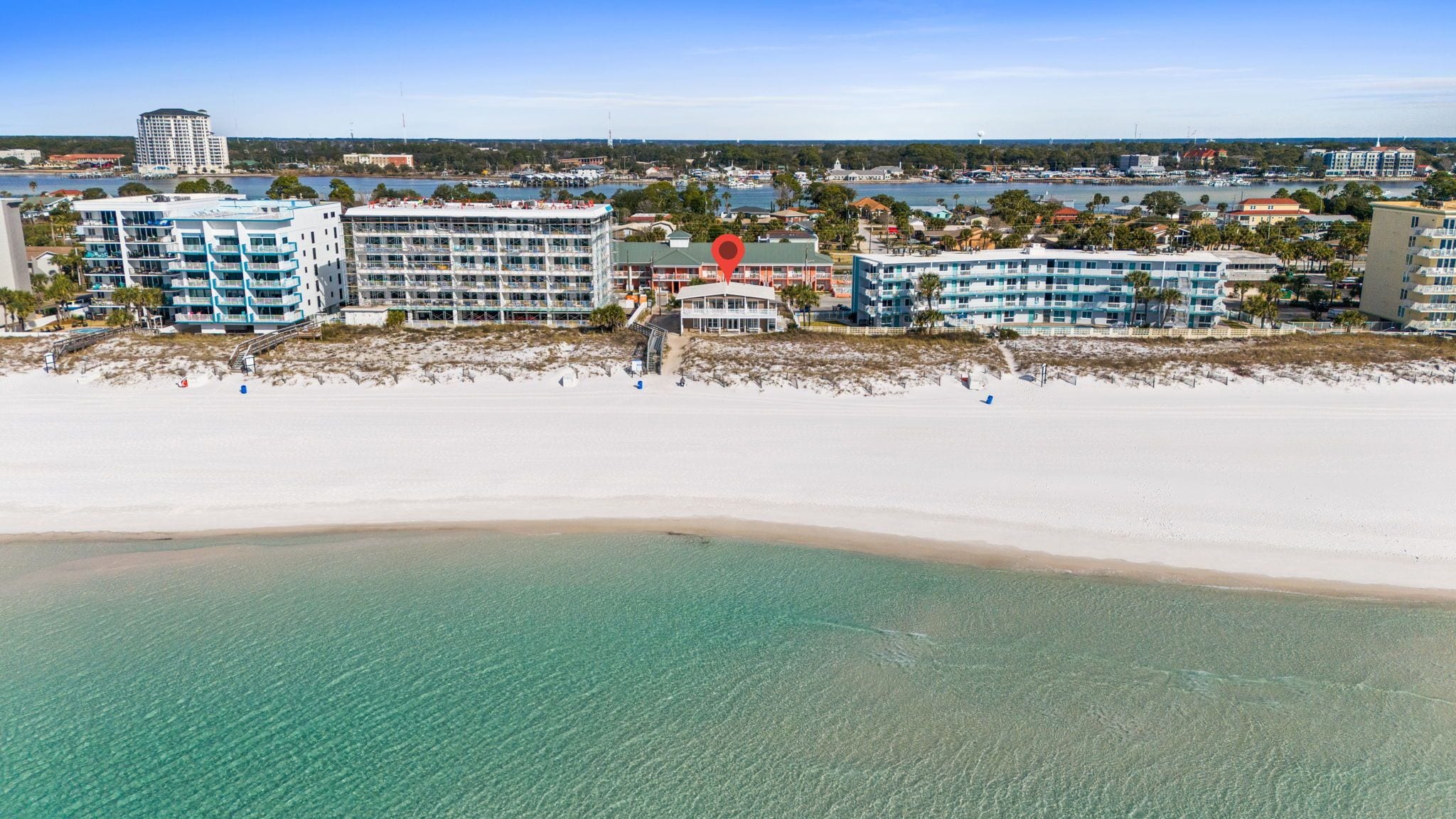Un hotel frente a la playa con varias edificaciones, una playa de arena y aguas cristalinas.