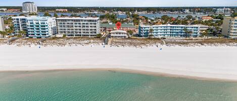 Un hotel frente a la playa con varias edificaciones, una playa de arena y aguas cristalinas.