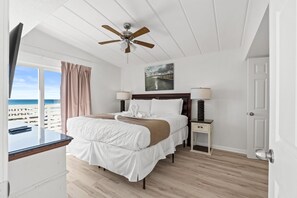 Egy hálószoba, amelyben található egy ágy, egy mennyezeti ventilátor, egy éjjeliszemélyzet, egy lámpa, egy televízió, és kilátás nyílik az óceánra.