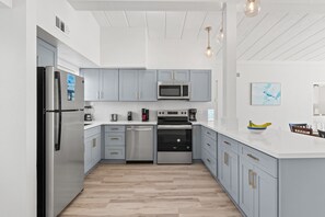 A modern kitchen with grey cabinets, stainless steel appliances, and a white countertop. - Coconut Beach House A (Fort Walton Beach)