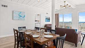A dining area with a wooden table and chairs, a brown sofa, and a view of the ocean through large windows. - Coconut Beach House A (Fort Walton Beach)