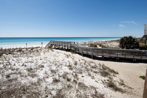 A beach with a wooden boardwalk leading to the water, sandy dunes, and a clear blue sky. - Coconut Beach House A (Fort Walton Beach)